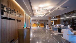 Um saguão moderno de hotel, com balcão de recepção, área de estar e prateleiras decorativas.