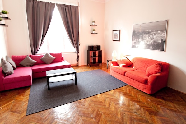A living room with a red sofa, a black coffee table, and a red couch. There is a black rug on the floor, a window with curtains, and a picture on the wall.