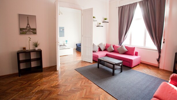 A modern living room with a herringbone floor, a pink sofa, a coffee table, and a view of the Eiffel Tower through a window. - Budapest Easy Flat - Wesselenyi Apartment (Budapest)