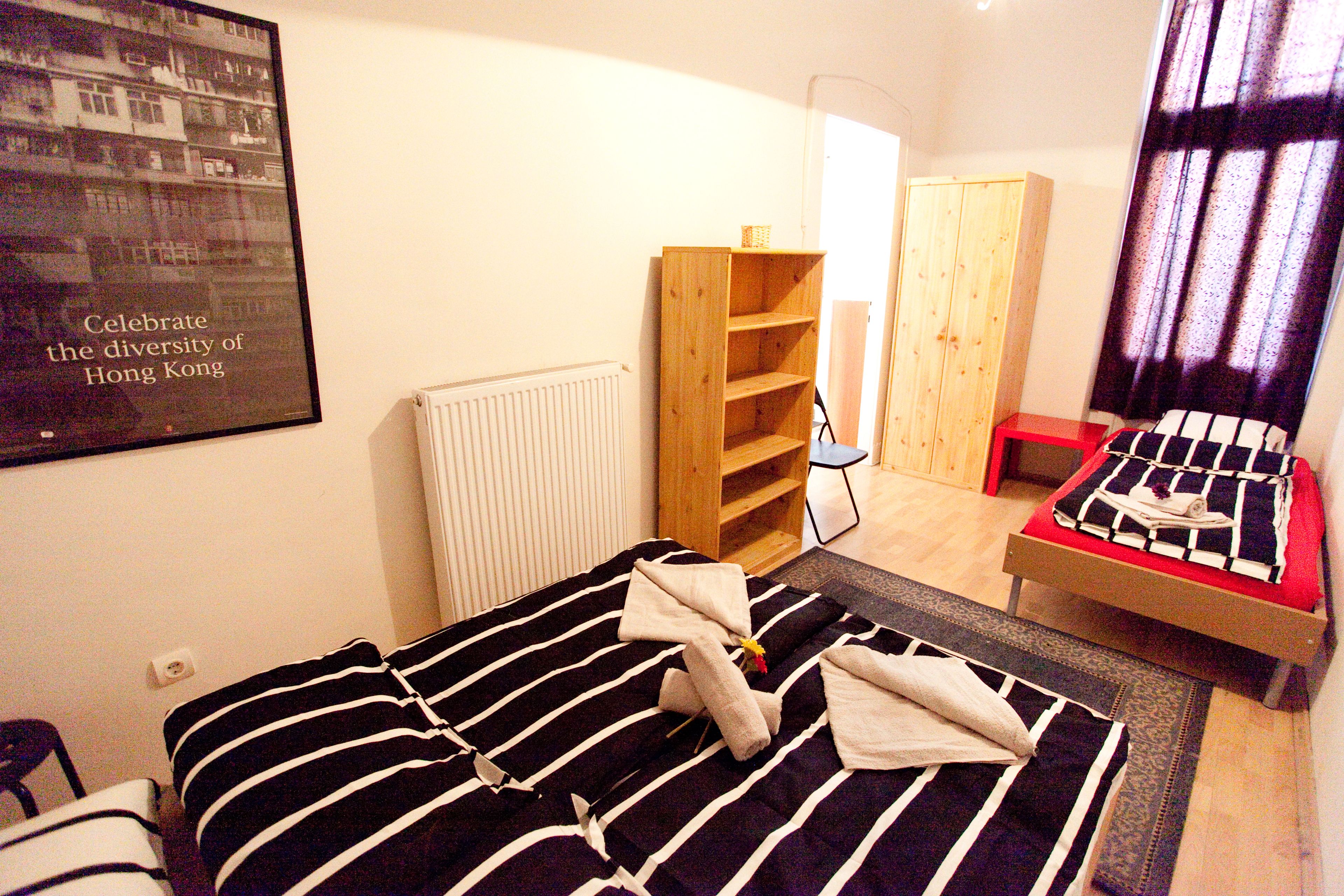 A hotel room with a bed, a wooden shelf, a red chair, and a poster on the wall.