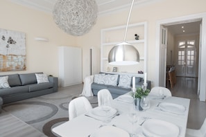 Una sala moderna con comedor, que presenta un gran comedor listo para seis personas, un sofá gris y una lámpara de araña blanca.