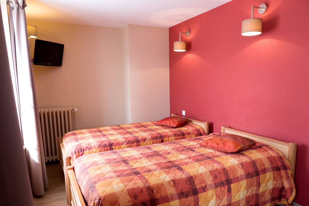 Ein Schlafzimmer mit zwei Betten, einem an der Wand befestigten Fernseher und einer Heizung.