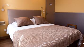 Una habitación de hotel con una cama, una mesita de noche, una lámpara y una puerta.