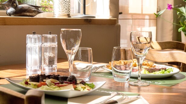 Une table à manger avec des assiettes remplies de nourriture, des verres et des salières.