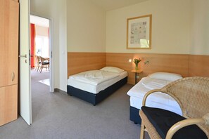 Habitación de hotel con dos camas, cabecera de madera, mesita de noche pequeña con una lámpara y un cuadro enmarcado en la pared.