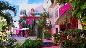 A vibrant courtyard with a pink building, outdoor seating, and lush greenery. - Santuario Playa (Playa del Carmen)