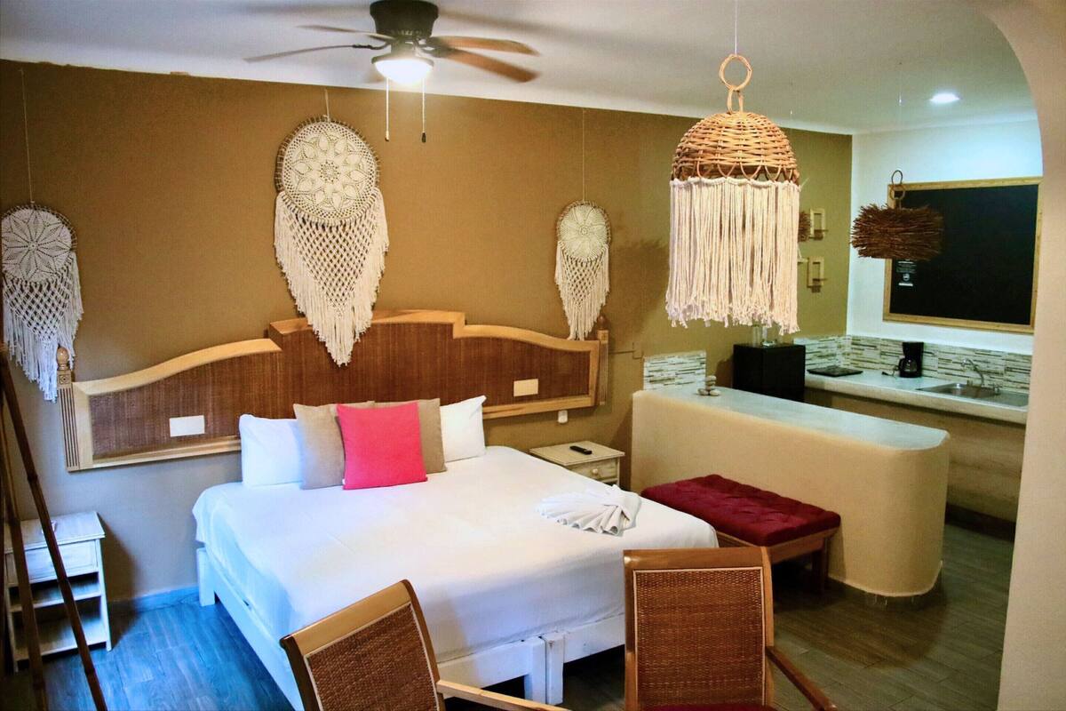 Een hotelkamer met een bed, nachtkastjes, een bureau, een stoel, een hangende macramé lamp en een plafondventilator.
