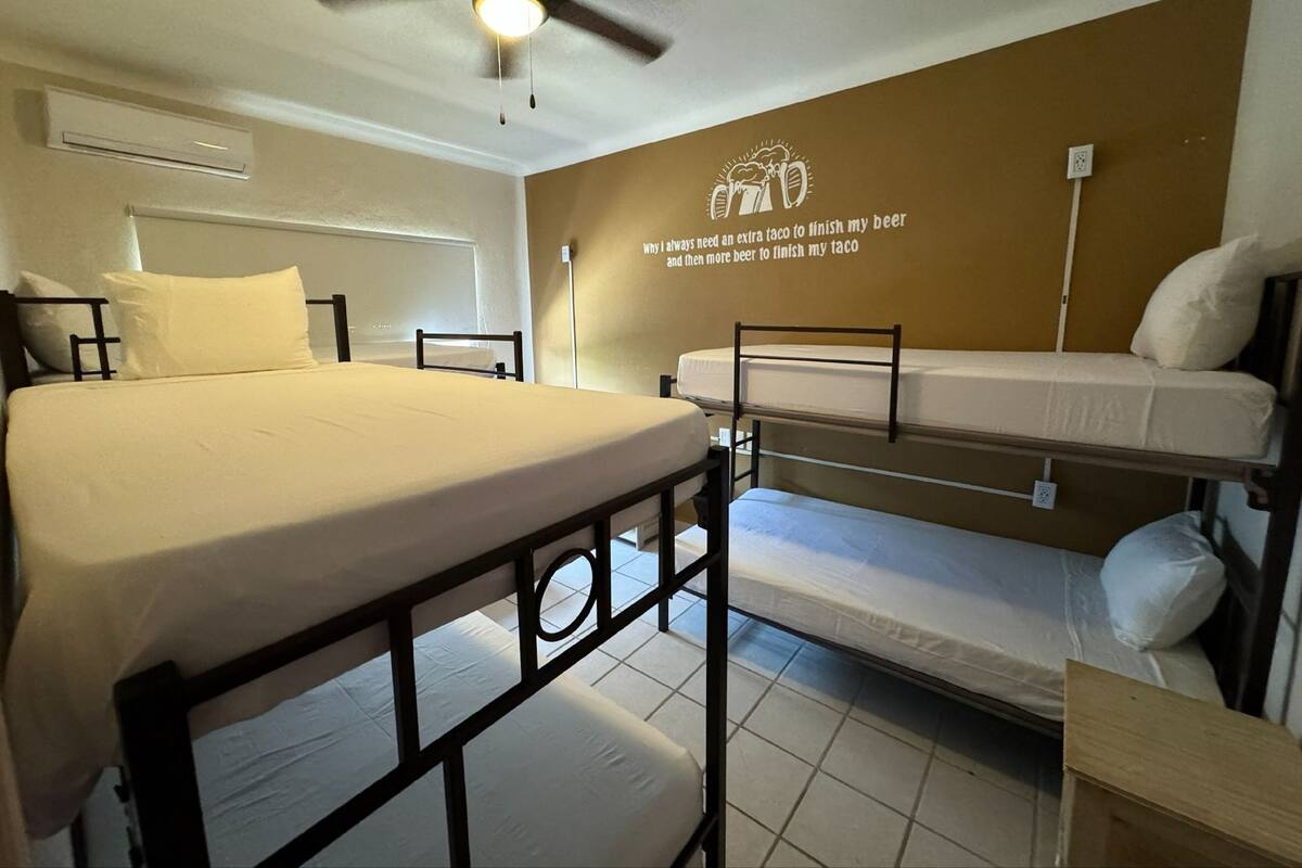 Een slaapzaal met een enkel bed, een stapelbed en een plafondventilator.