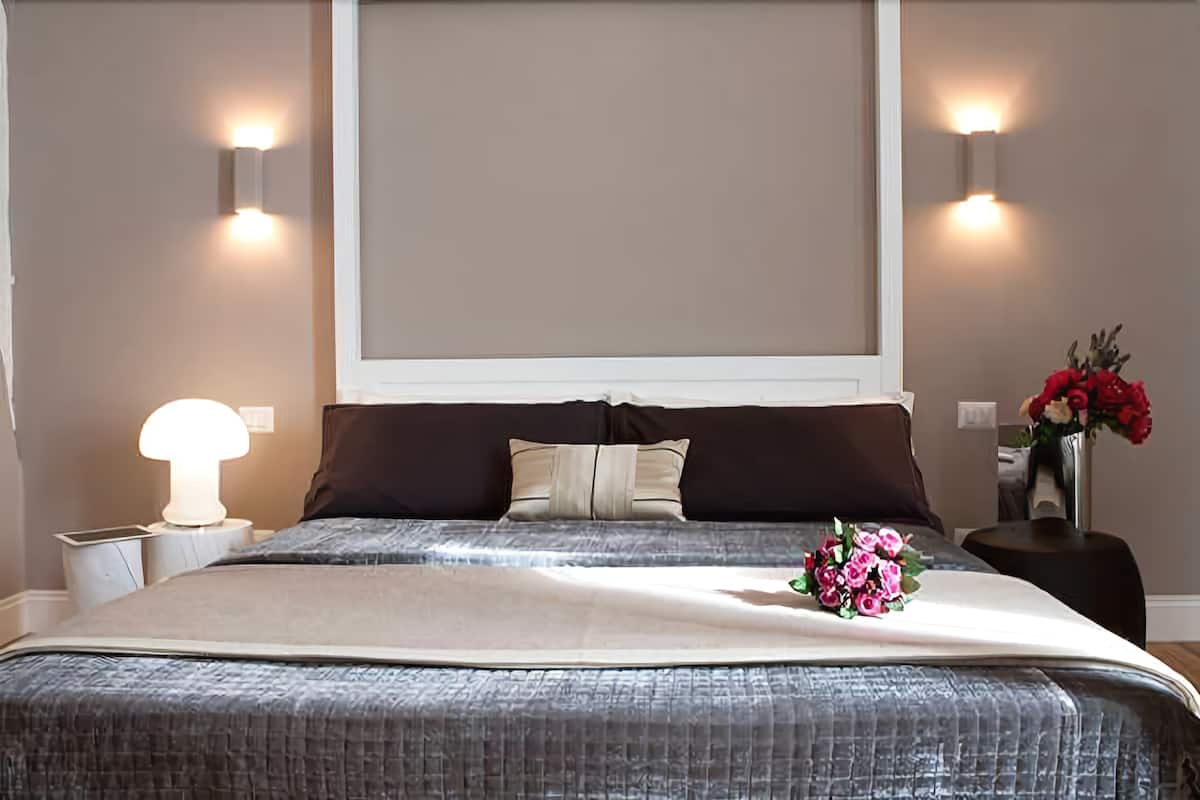 A neatly made bed with a decorative flower arrangement, two bedside lamps, and a vase with flowers on a nightstand.