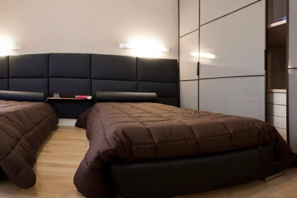 A modern bedroom with two beds, a large headboard, and built-in storage.