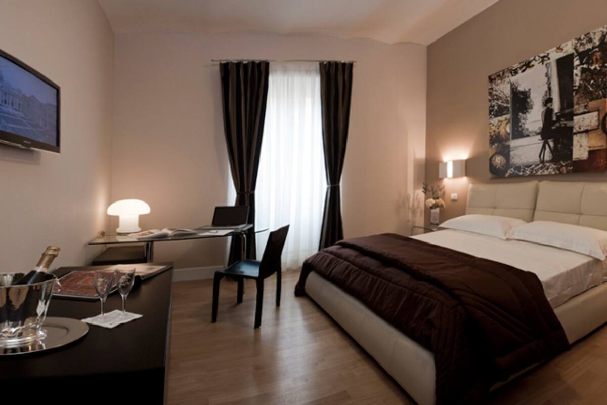 A modern hotel room with a bed, desk, chair, and a large painting on the wall.
