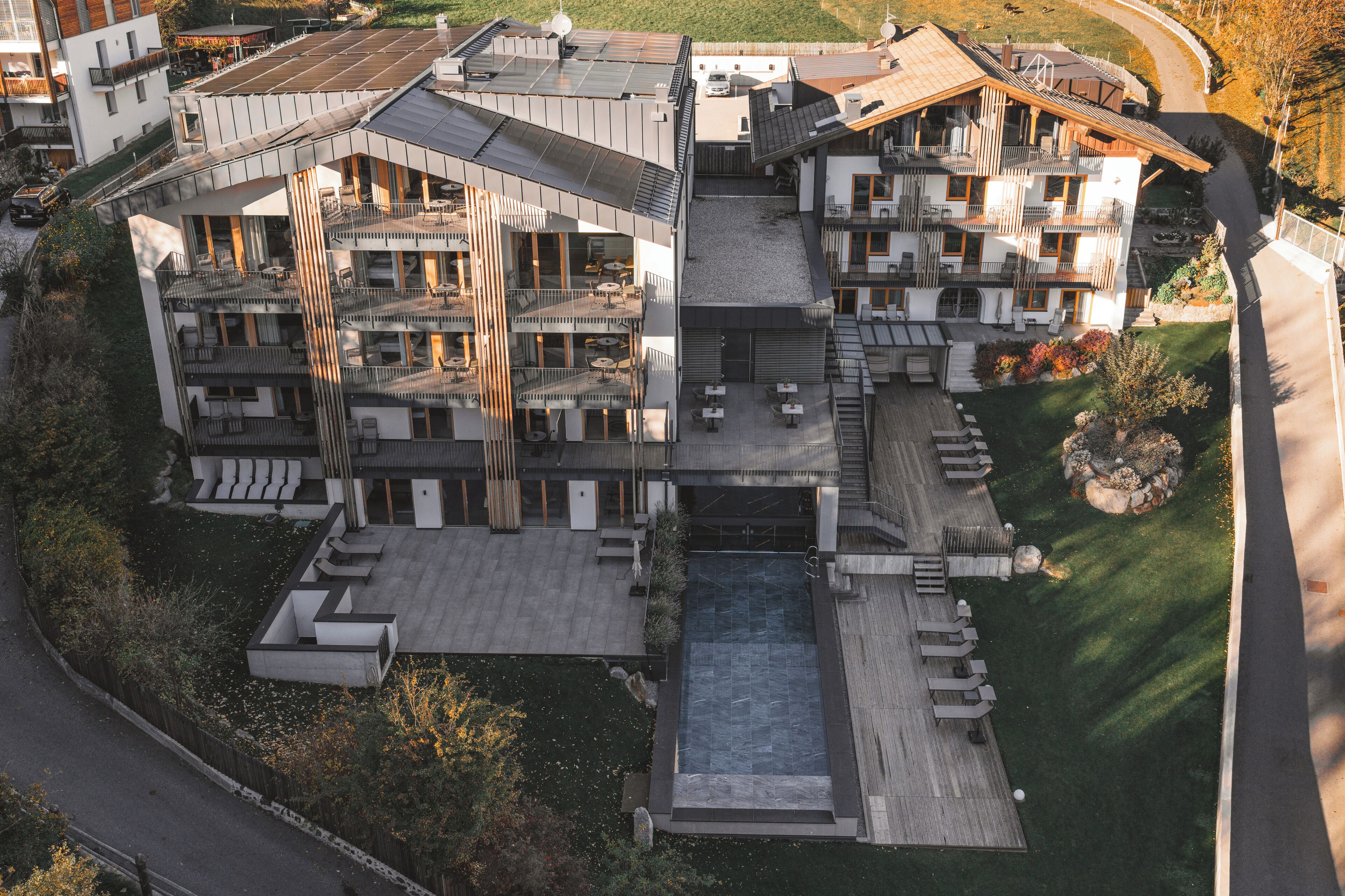 A modern multi-story building with a rooftop pool, outdoor seating, and a landscaped garden.