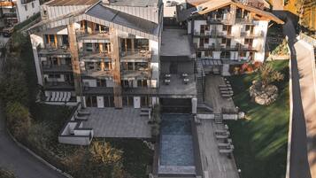 A modern multi-story building with a rooftop pool, outdoor seating, and a landscaped garden.