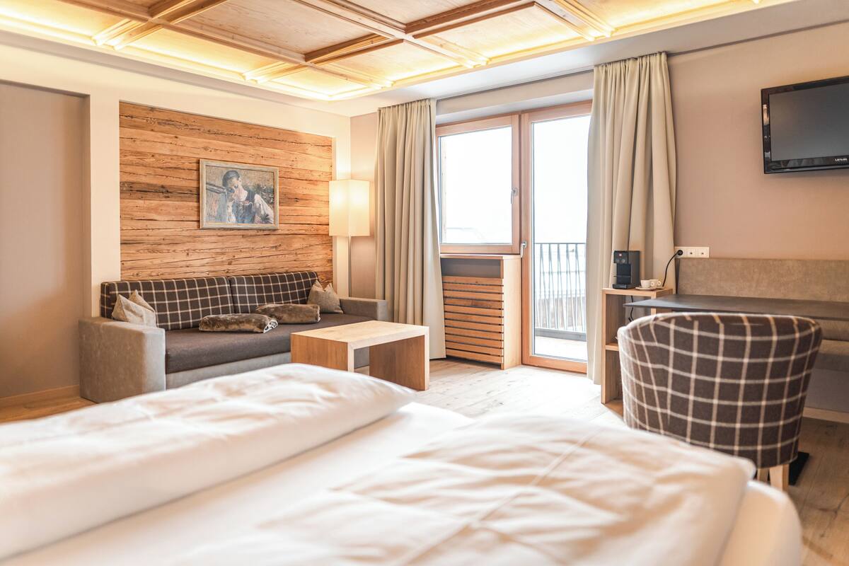 Une chambre d’hôtel avec un grand lit, un canapé, une petite table, une chaise, une télévision et un balcon avec des rideaux.