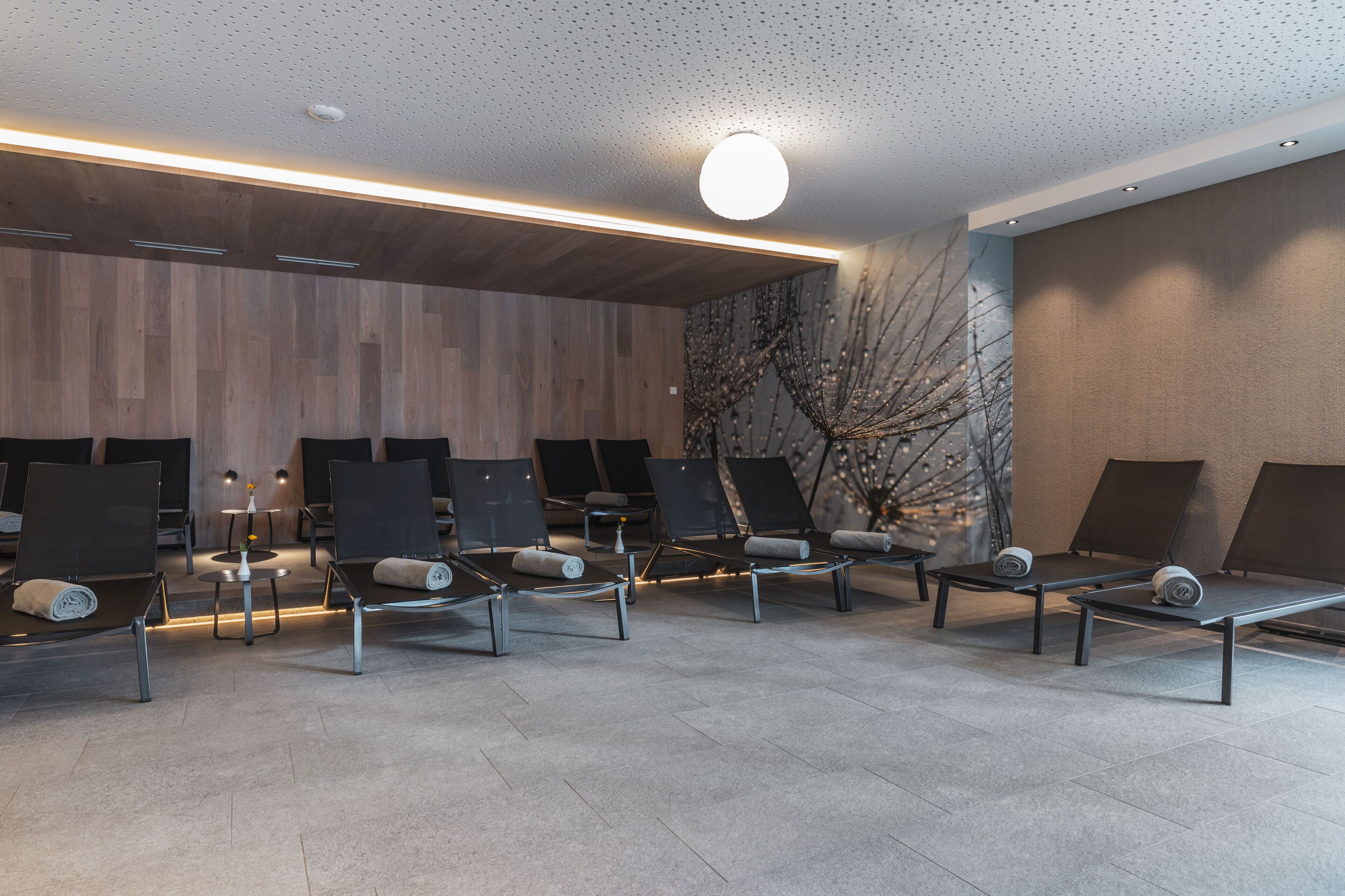 Un área de espera moderna con varias sillas de descanso, un muro de madera y una planta decorativa.