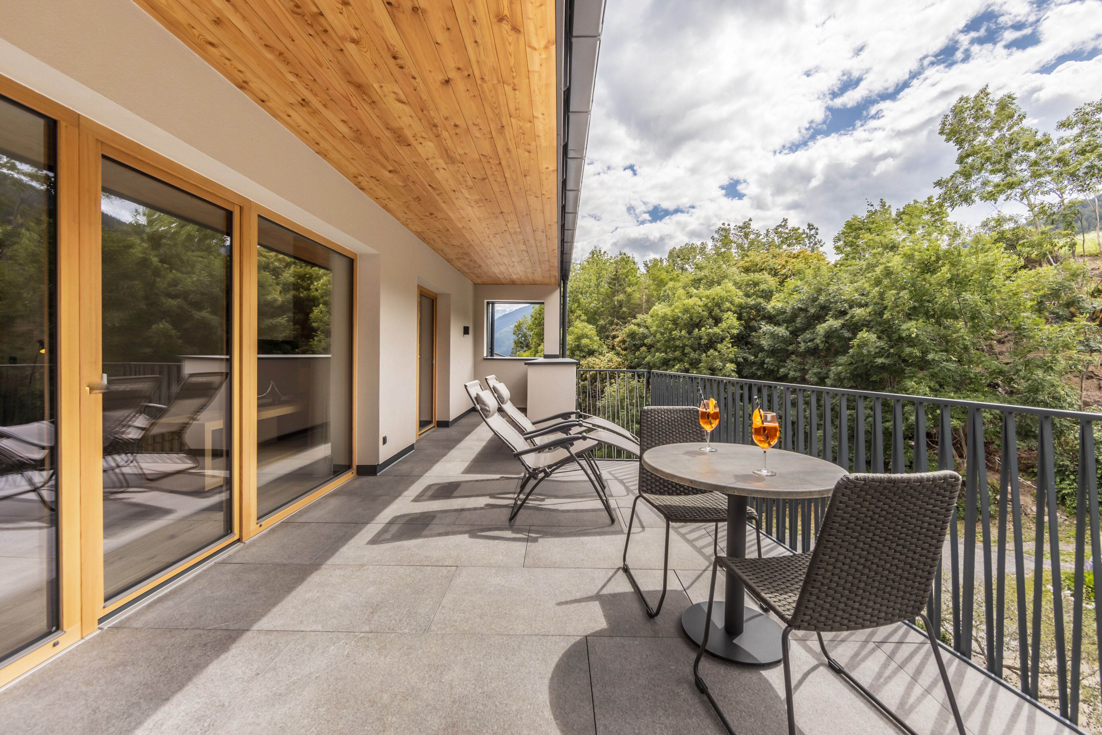 A balcony with a wooden ceiling, glass doors, and a table with chairs and a glass of wine.