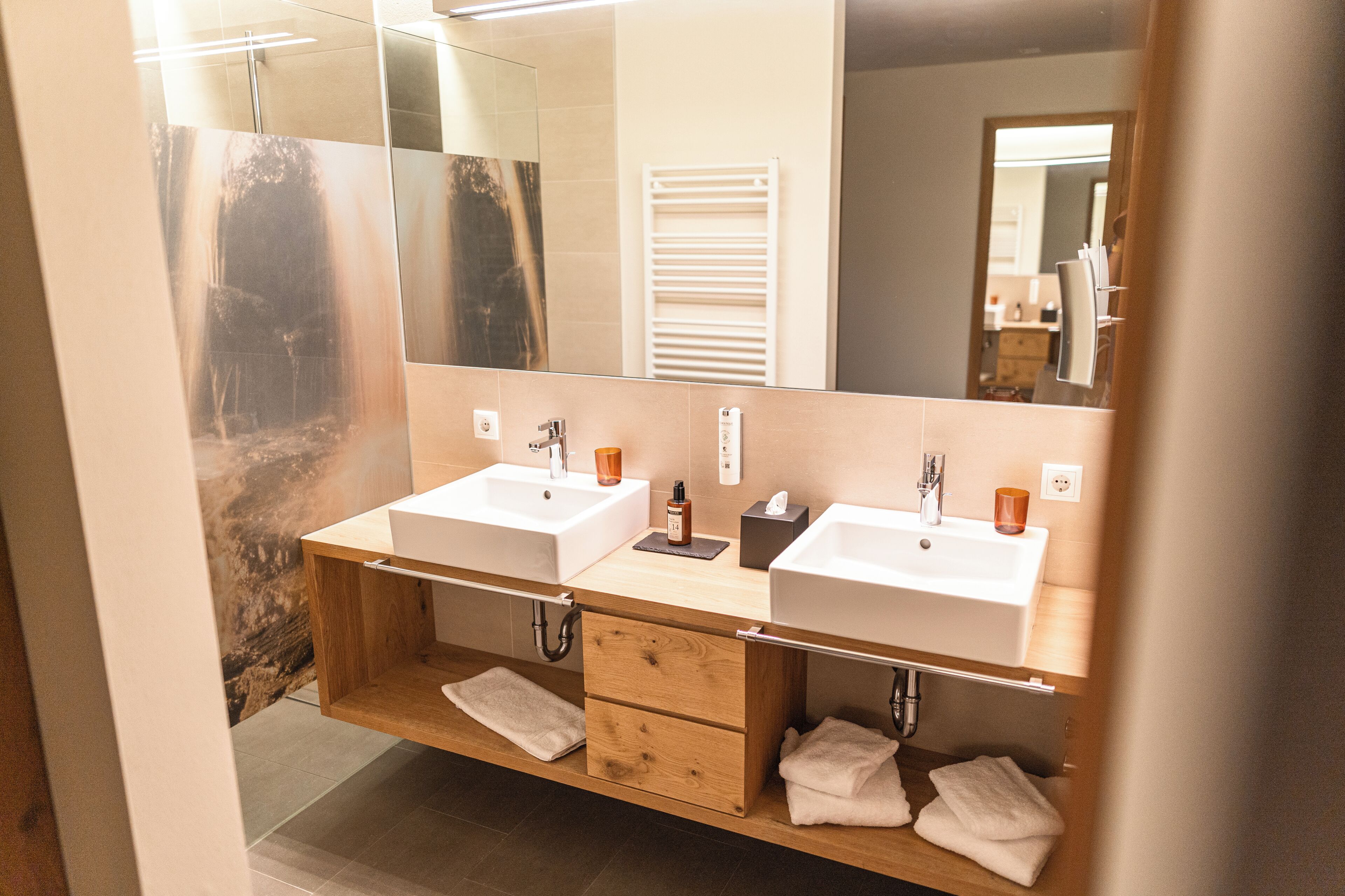 A modern bathroom with two sinks, a large mirror, and a wooden vanity with drawers.