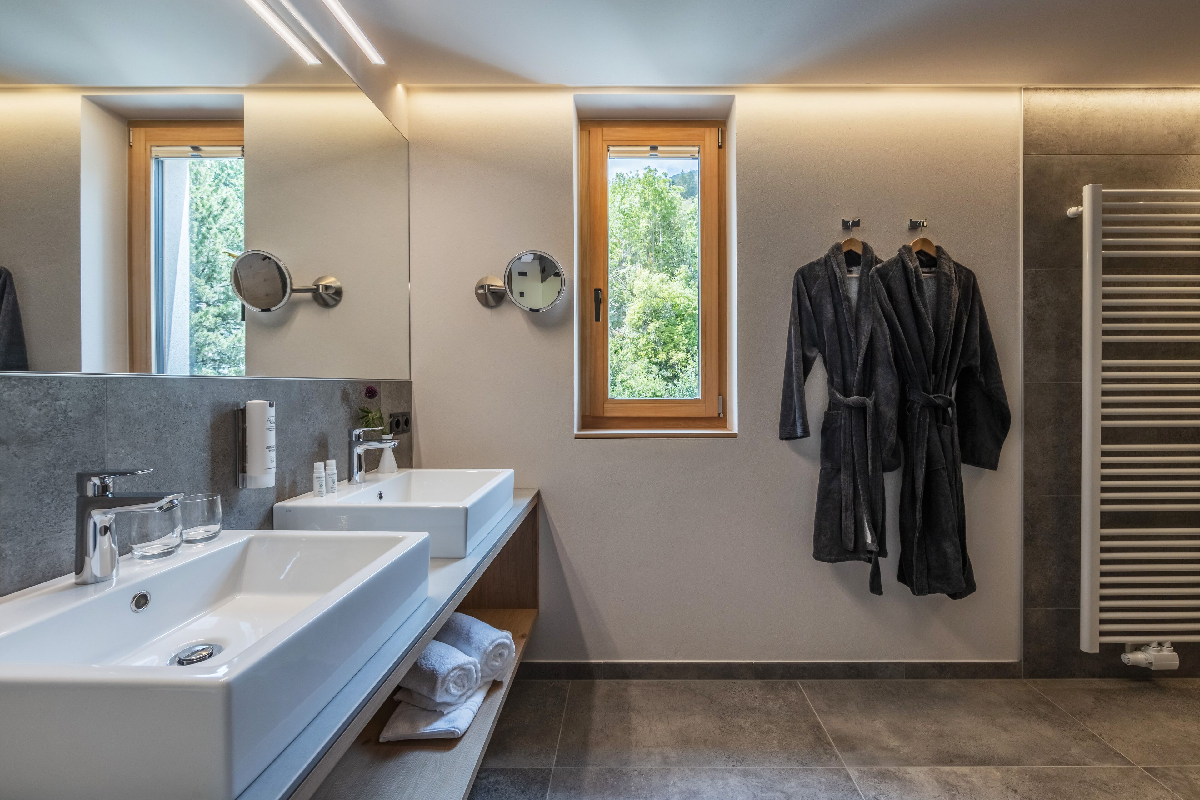 A modern bathroom with two sinks, a mirror, and a window.