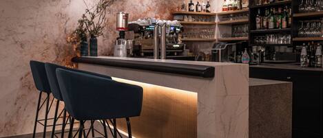 Un espace bar moderne avec un mur en marbre, un comptoir doté d’un panneau lumineux et des tabourets de bar.