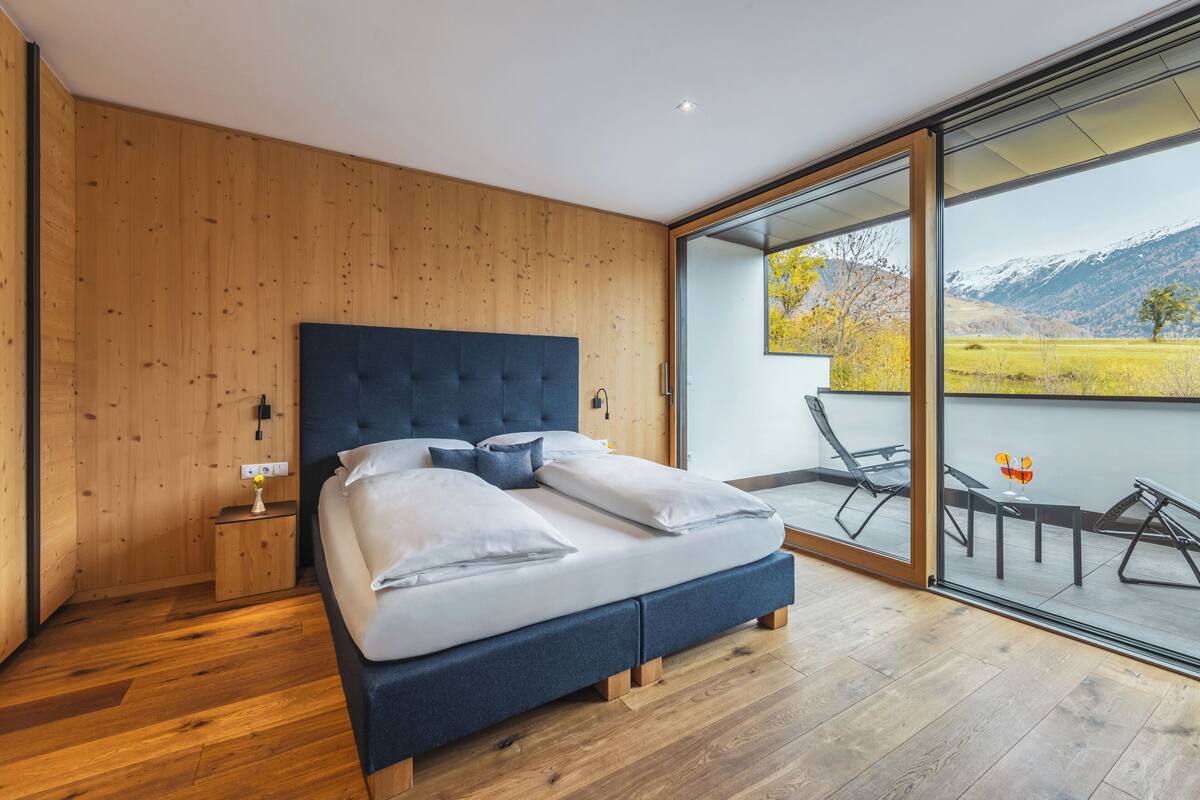 Une chambre moderne avec un grand lit, des murs en bois et une porte en verre donnant sur un espace de détente extérieur avec vue sur la montagne.