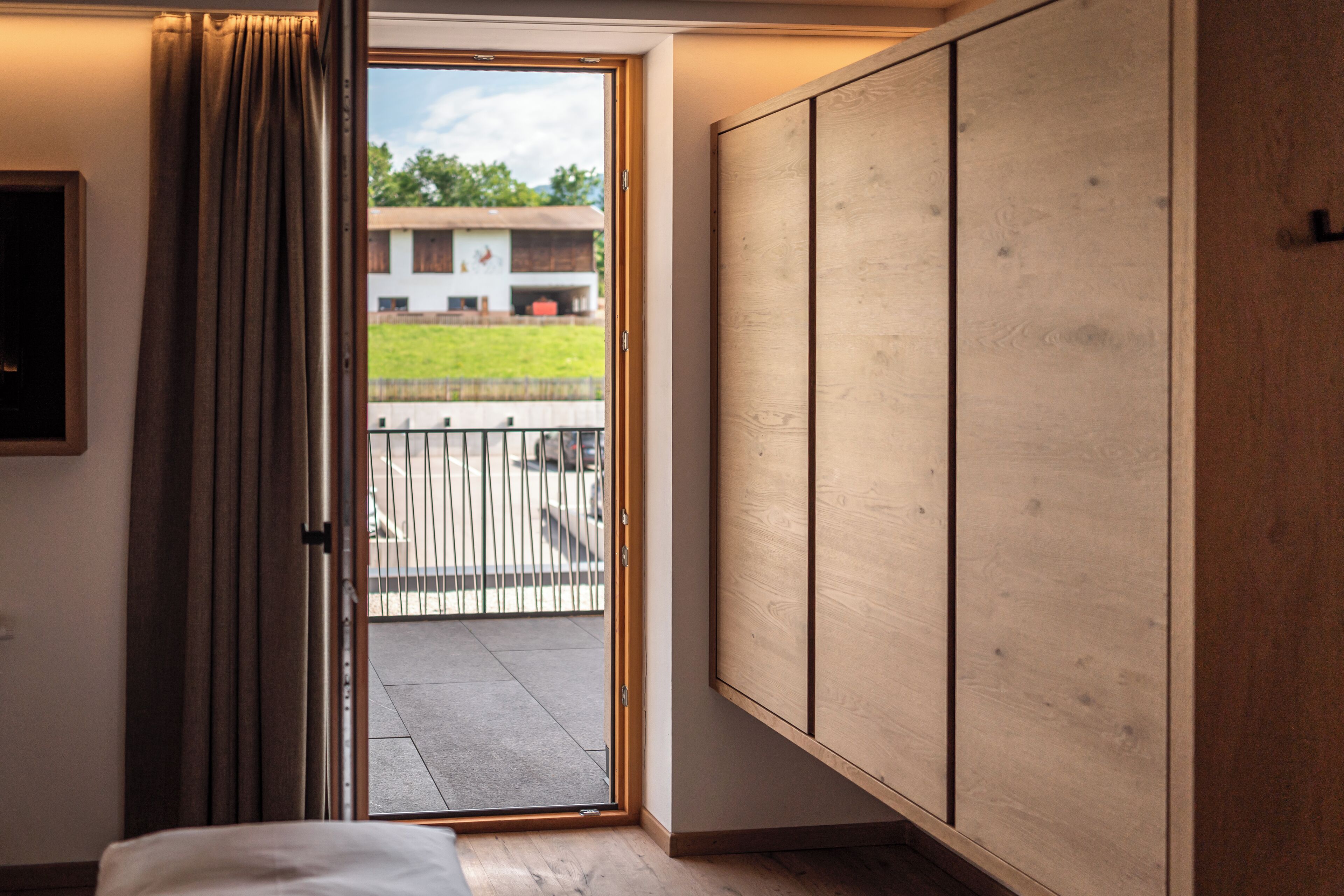 Habitación de hotel con armario de madera, cama y puerta corrediza de vidrio que da a un balcón exterior.