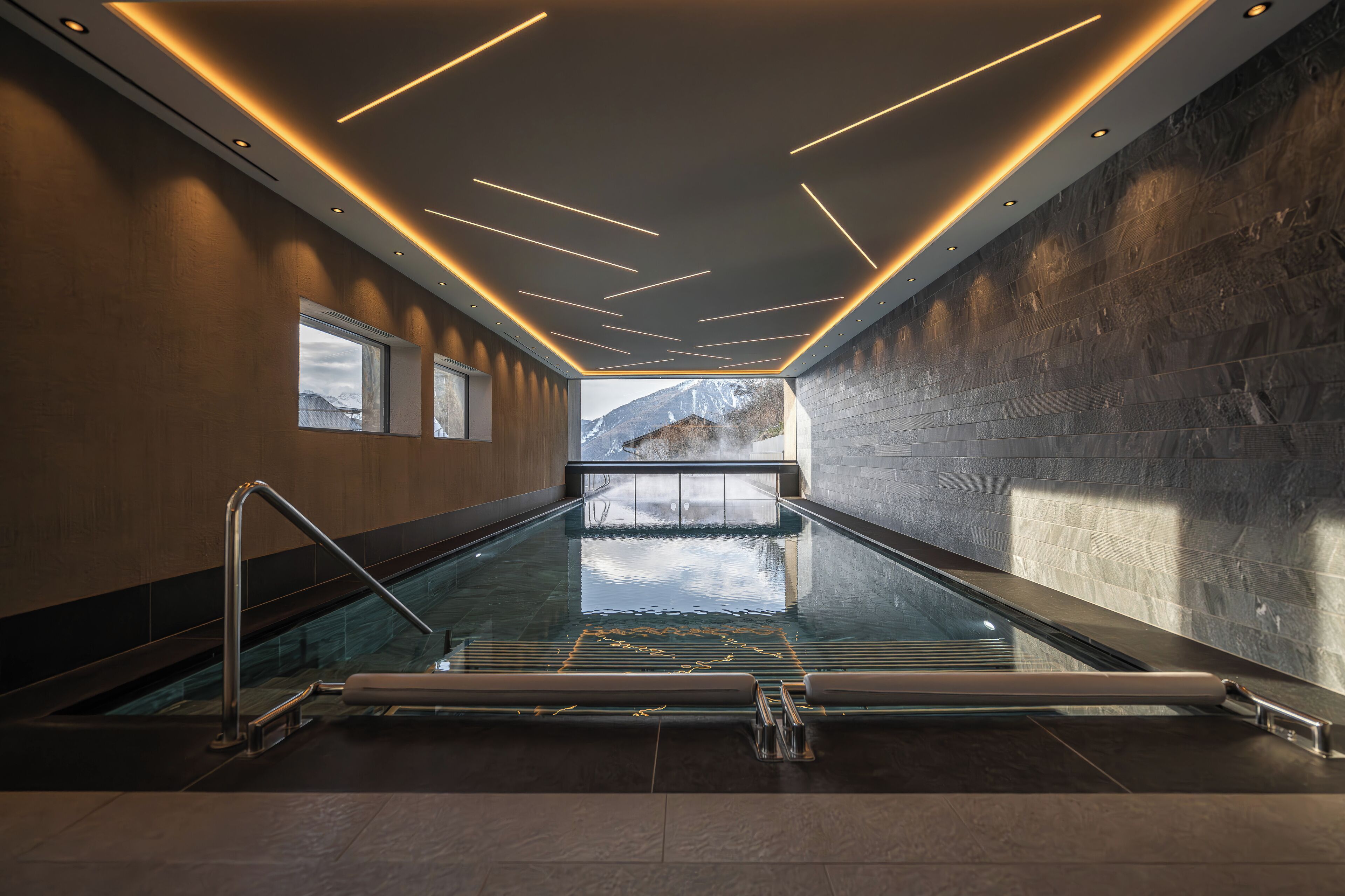 A modern indoor swimming pool with a view of mountains, sleek lighting, and a minimalist design.