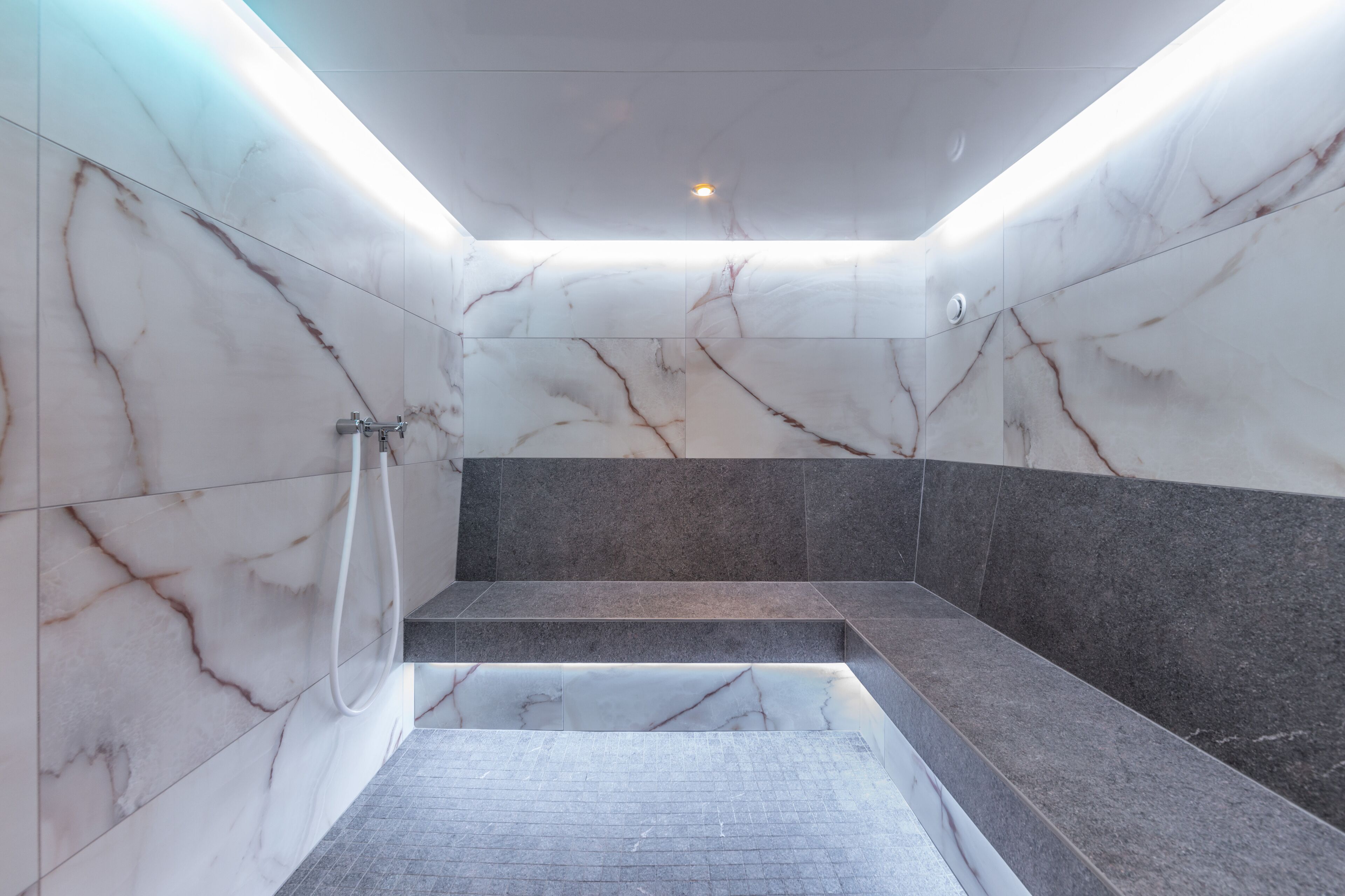 A modern bathroom with marble walls, a built-in bench, and a shower area.