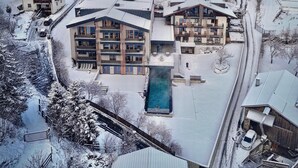 Un complejo turístico cubierto de nieve con varias edificaciones, una piscina y una pista de esquí al fondo.