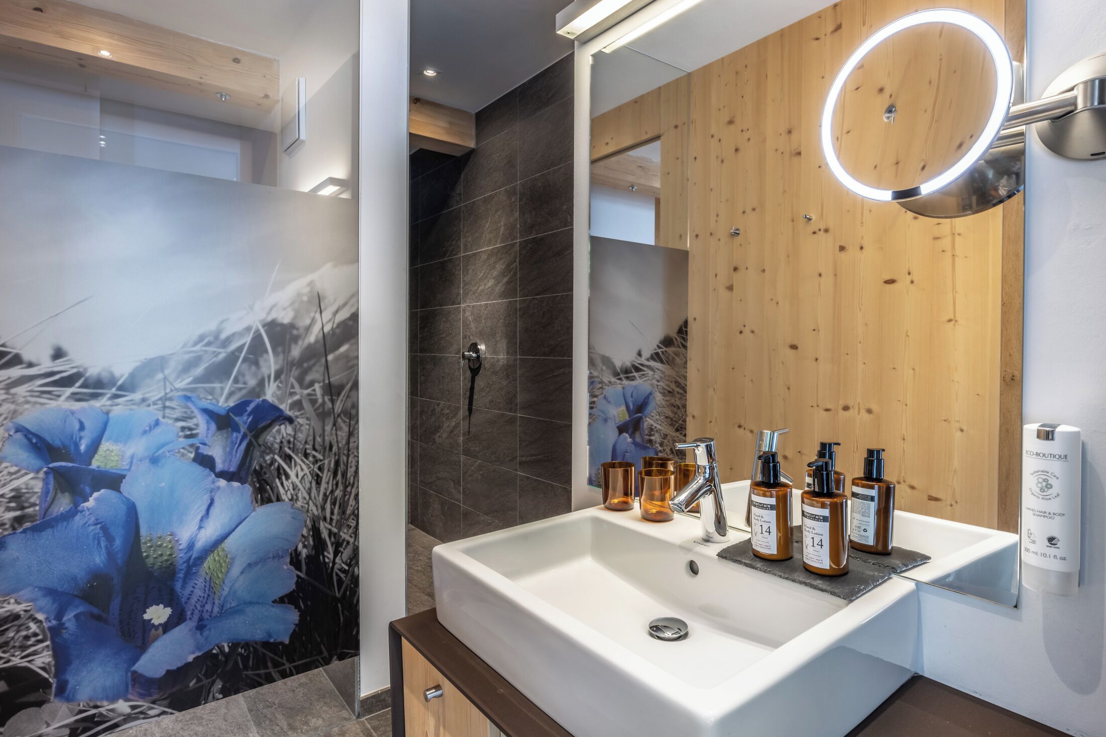 A modern bathroom with a white sink, wooden panel wall, and a mirror with a light.