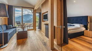 Una habitación de hotel moderna con cama, televisor, sofá y balcón con vista a la montaña.