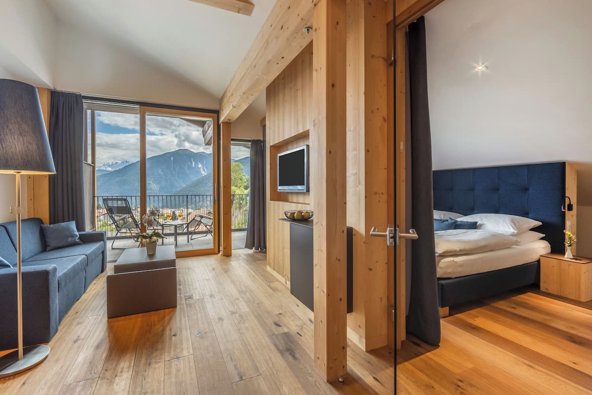 Une chambre d’hôtel moderne équipée d’un lit, d’une télévision, d’un canapé et d’un balcon offrant une vue sur la montagne.