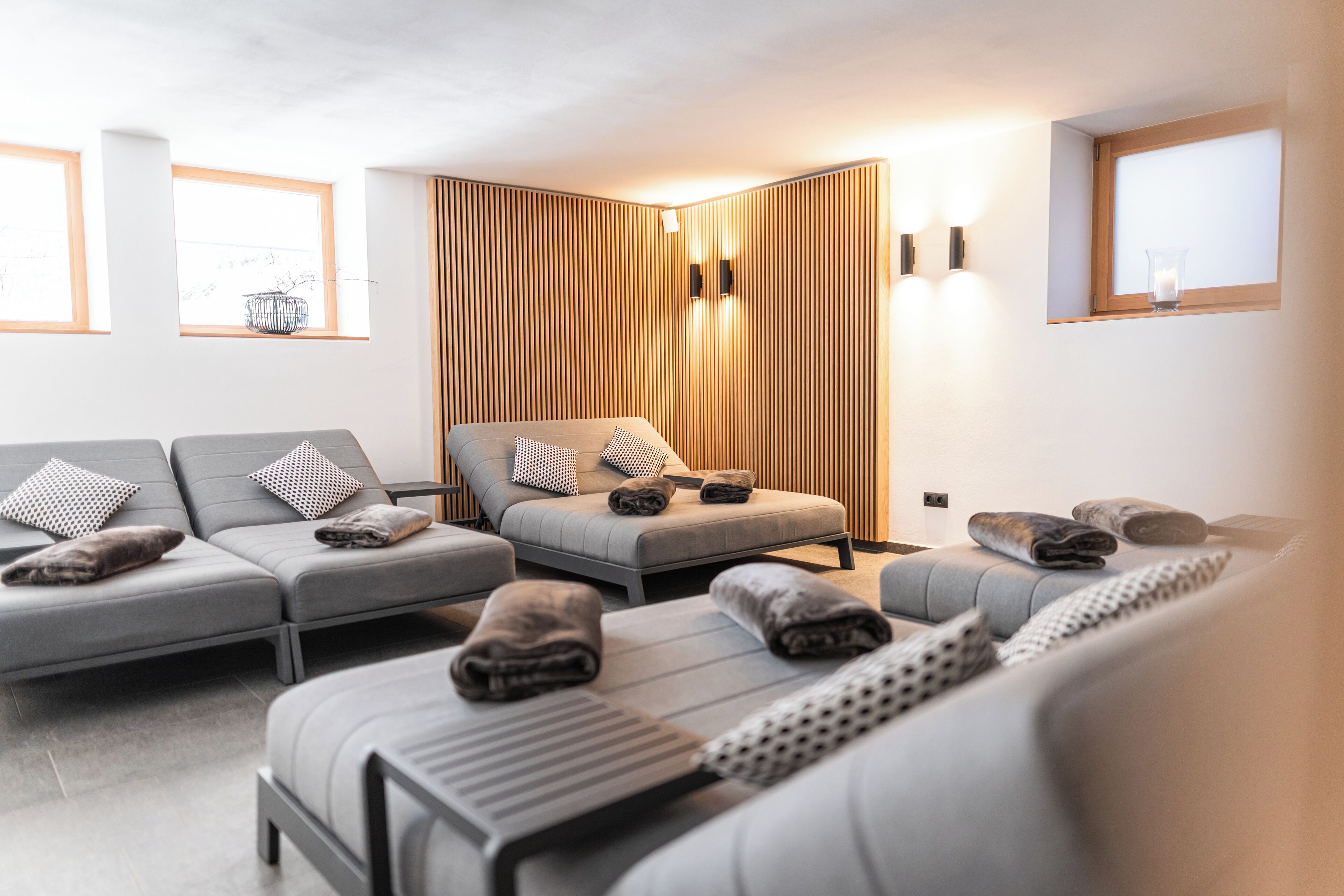 A modern spa room with a sofa, massage table, and a wooden panel wall.