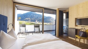 Un dormitorio con una cama grande, televisor, escritorio y sillas, y vistas a las montañas.
