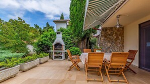 An outdoor patio with a stone fireplace, wooden chairs, and a table. - Luxurious home in Premantura (Premantura)