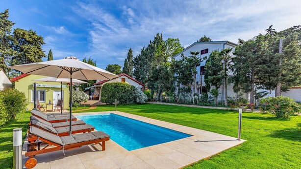 A swimming pool with lounge chairs and an umbrella, surrounded by a well-maintained lawn and trees. - Luxurious home in Premantura (Premantura)