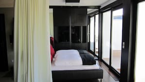 Une chambre à coucher moderne avec un grand lit, une porte-fenêtre coulissante et une vue sur l’extérieur.