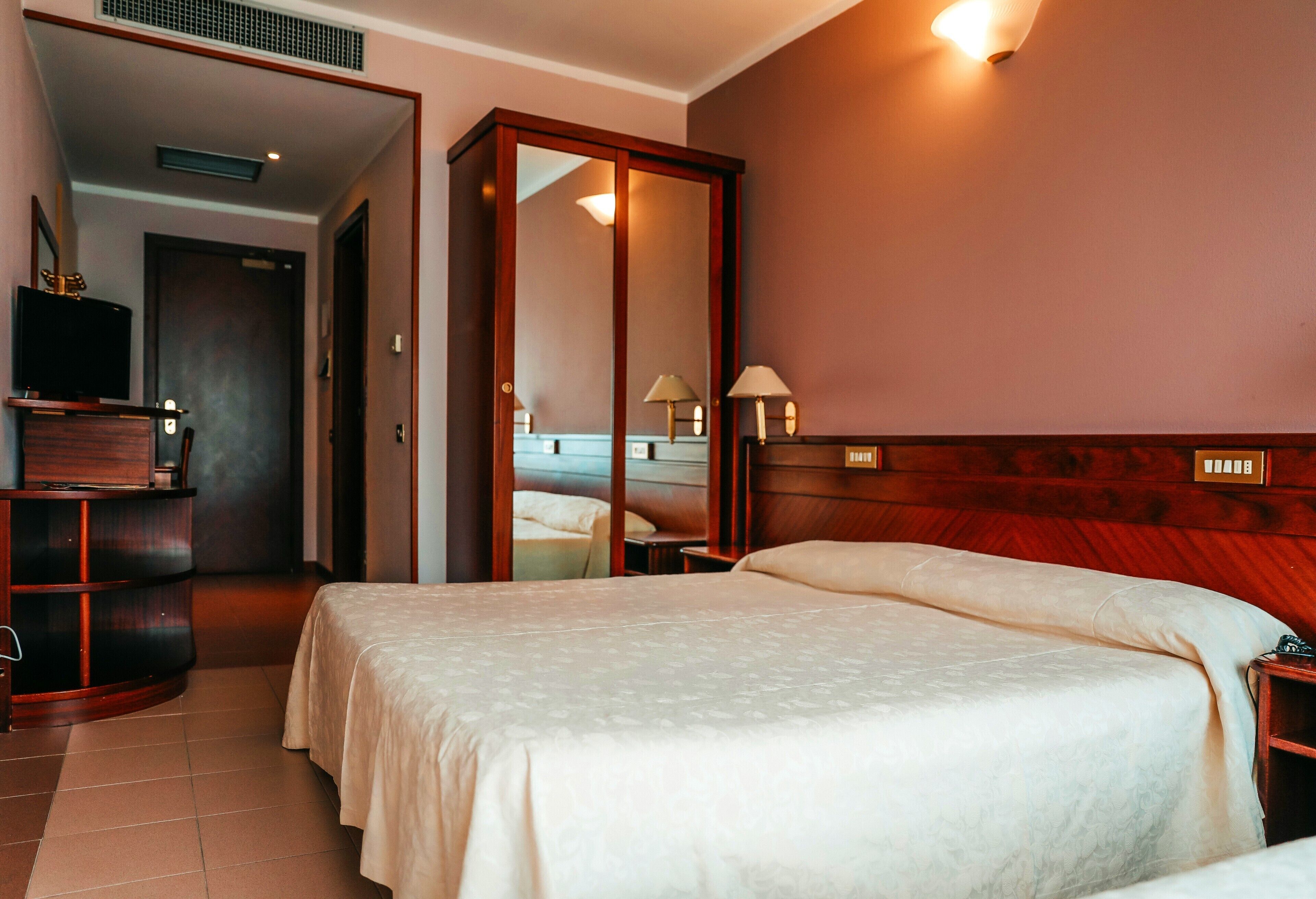 A hotel room with a bed, bedside tables, a wardrobe, a television, and a mirror.