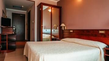 A hotel room with a bed, bedside tables, a wardrobe, a television, and a mirror.