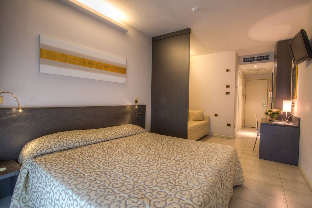 Une chambre d’hôtel avec un grand lit, un bureau avec une lampe, une télévision et un tableau au mur.