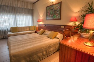 Habitación de hotel con dos camas, cabecero de madera, planta en maceta y dos lámparas.