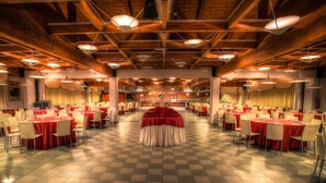 Un amplio salón de banquetes con varias mesas redondas cubiertas con manteles rojos y sillas blancas, vigas de madera en el techo y un suelo a cuadros.