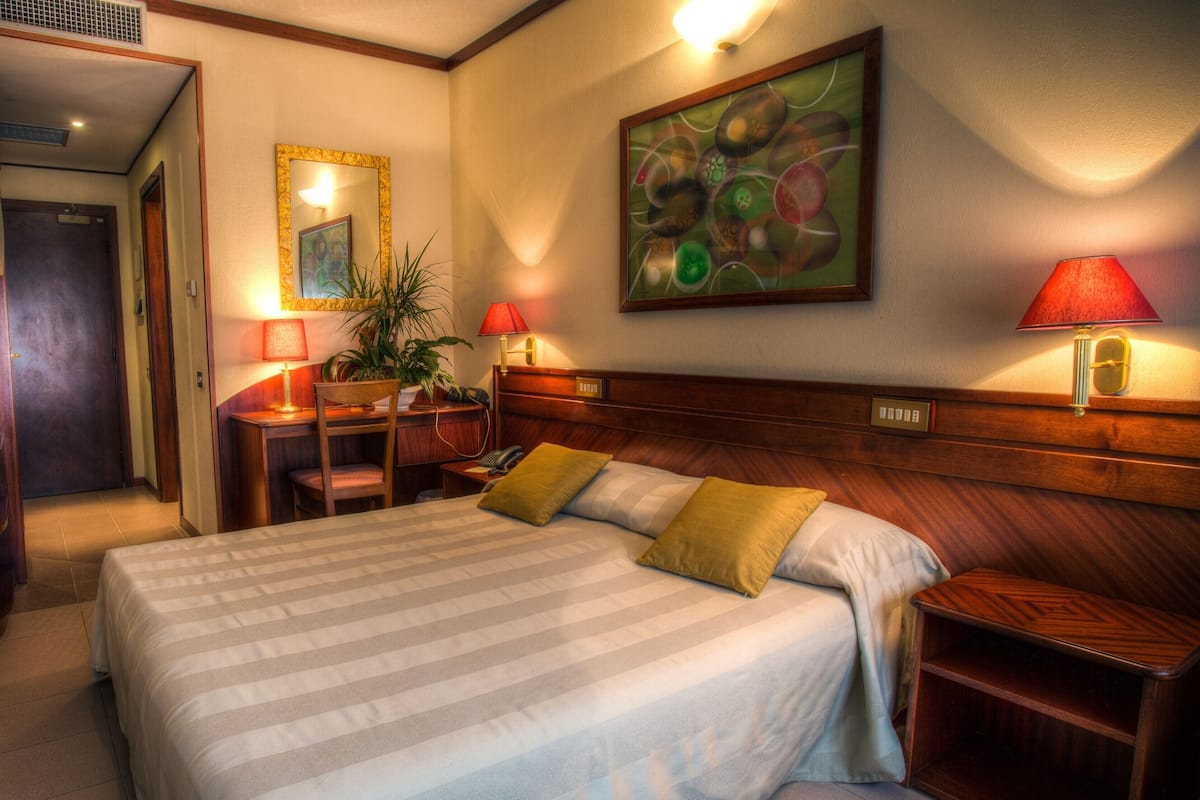 Une chambre d’hôtel avec un grand lit, des tables de chevet, un bureau avec une chaise, un miroir et un tableau au mur.