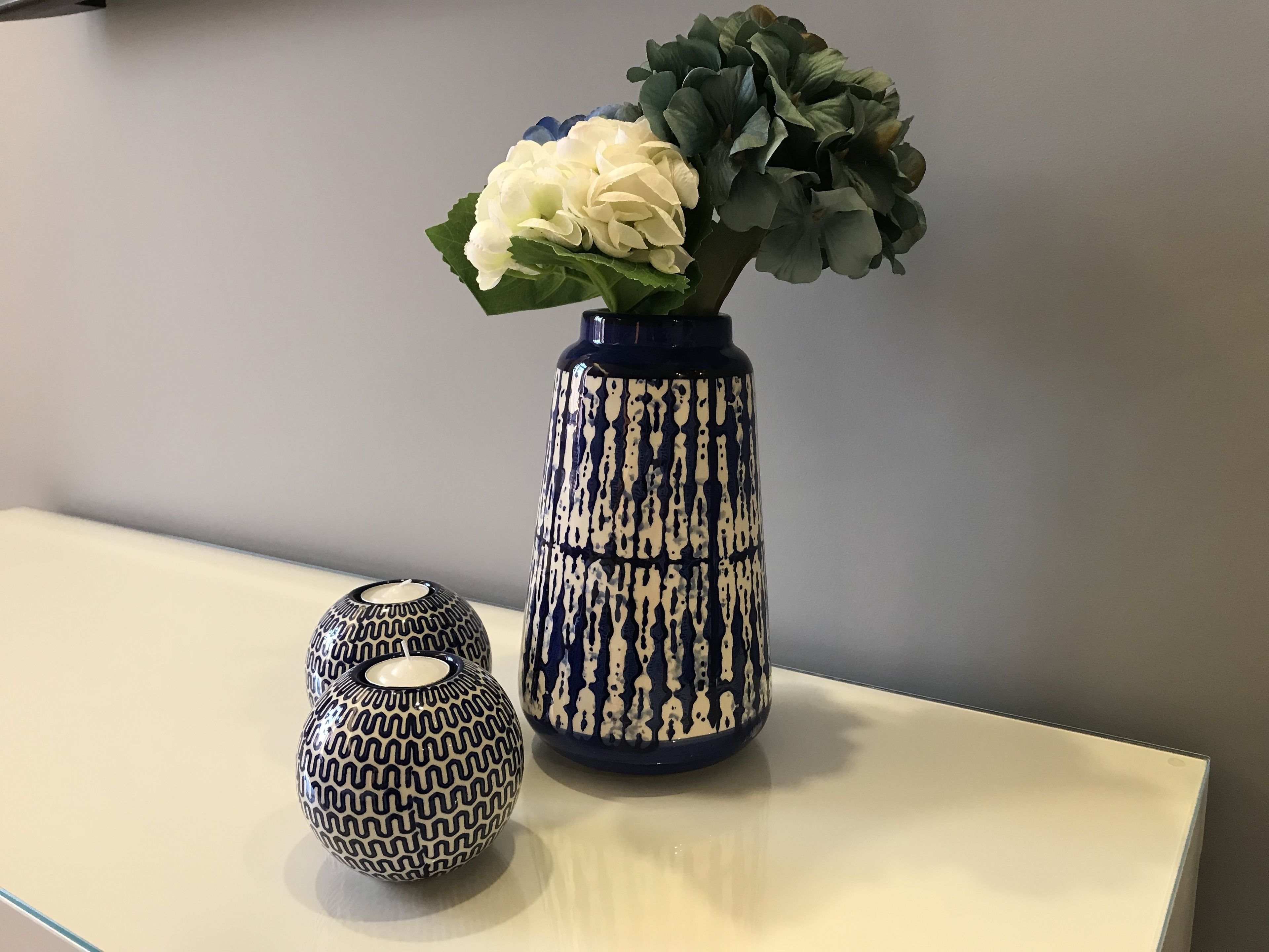 A vase with a blue and white pattern, a white flower, and a decorative object on a table.