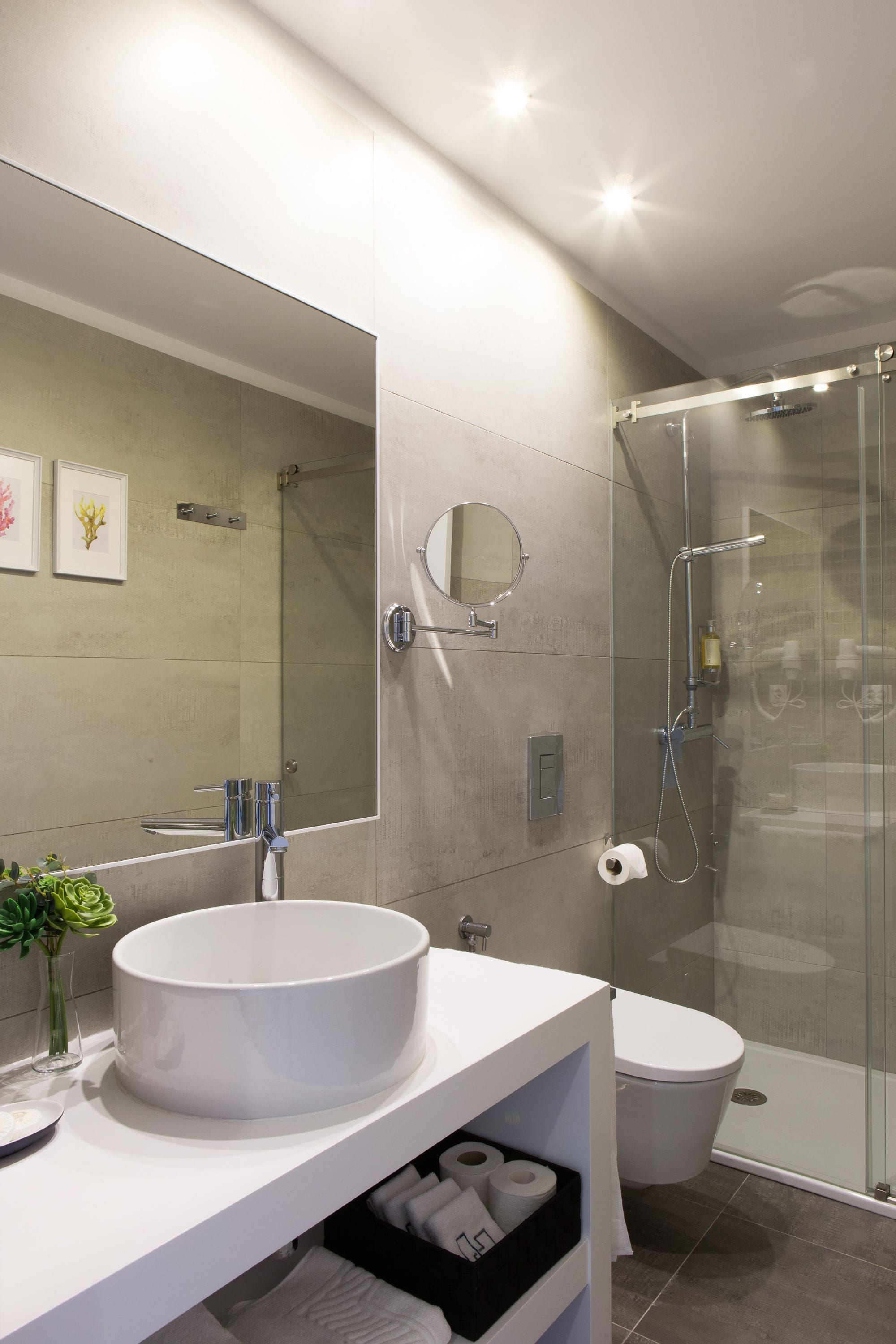 Un baño moderno con un espejo grande, un lavabo redondo, un inodoro y una ducha con mampara de vidrio.