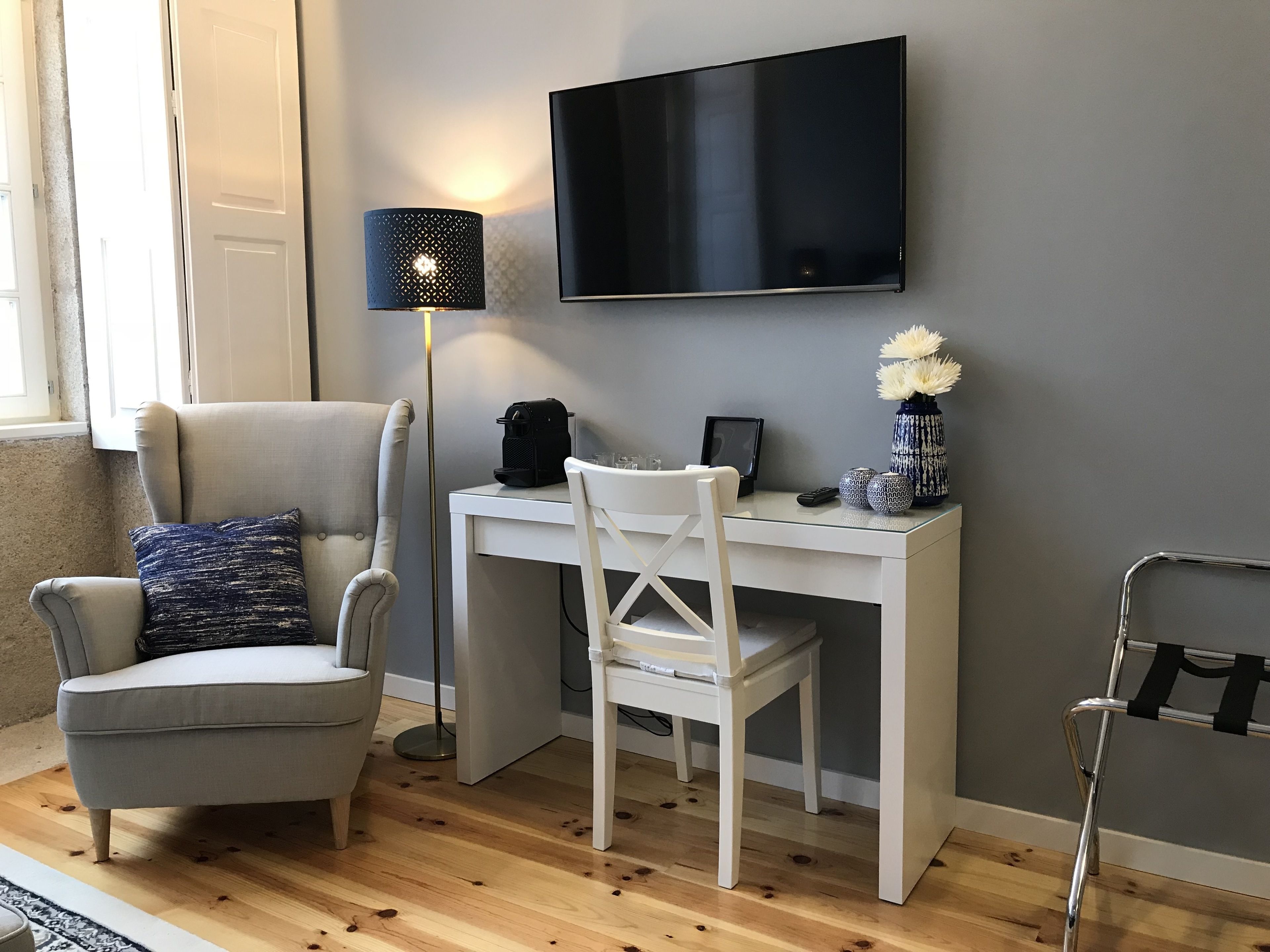En moderne stue med en grå sofa, et hvidt skrivebord og et fjernsyn ophængt på væggen.