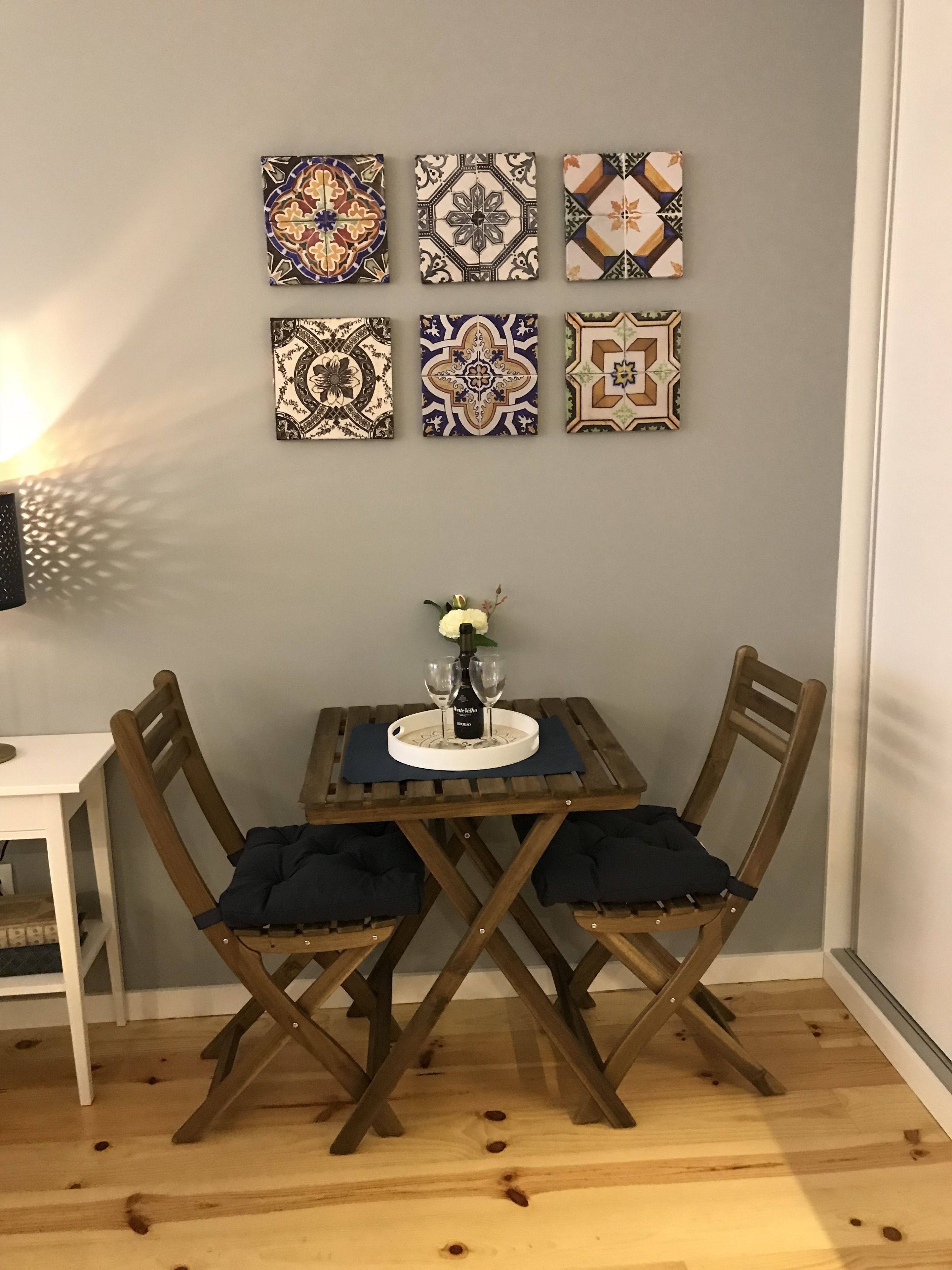 Un comedor con una mesa y sillas, una pared con azulejos decorativos y una mesita con un jarrón y vasos.