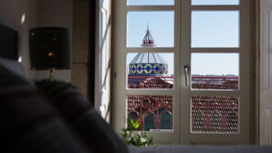 Een kamer met een groot raam dat uitkijkt op een kleurrijk gebouw met een opvallende dakconstructie.