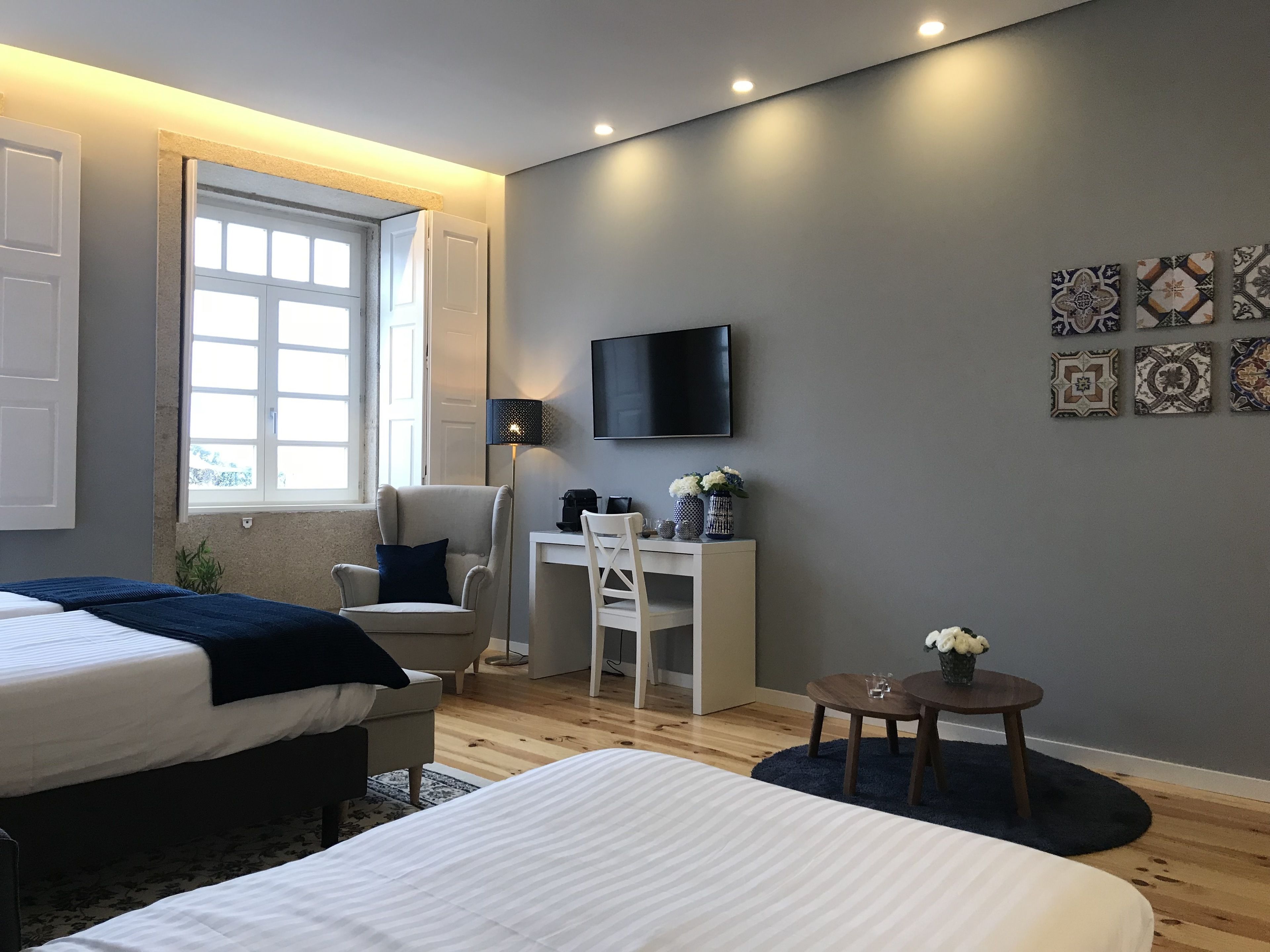 A modern bedroom with two beds, a desk, a chair, a TV, and decorative tiles on the wall.