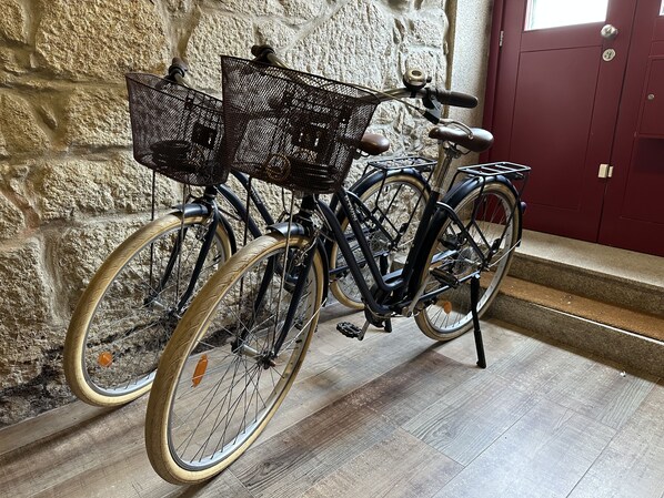 A bicycle with two baskets, parked against a stone wall with a wooden floor. - Virtudes City Lofts (Porto)