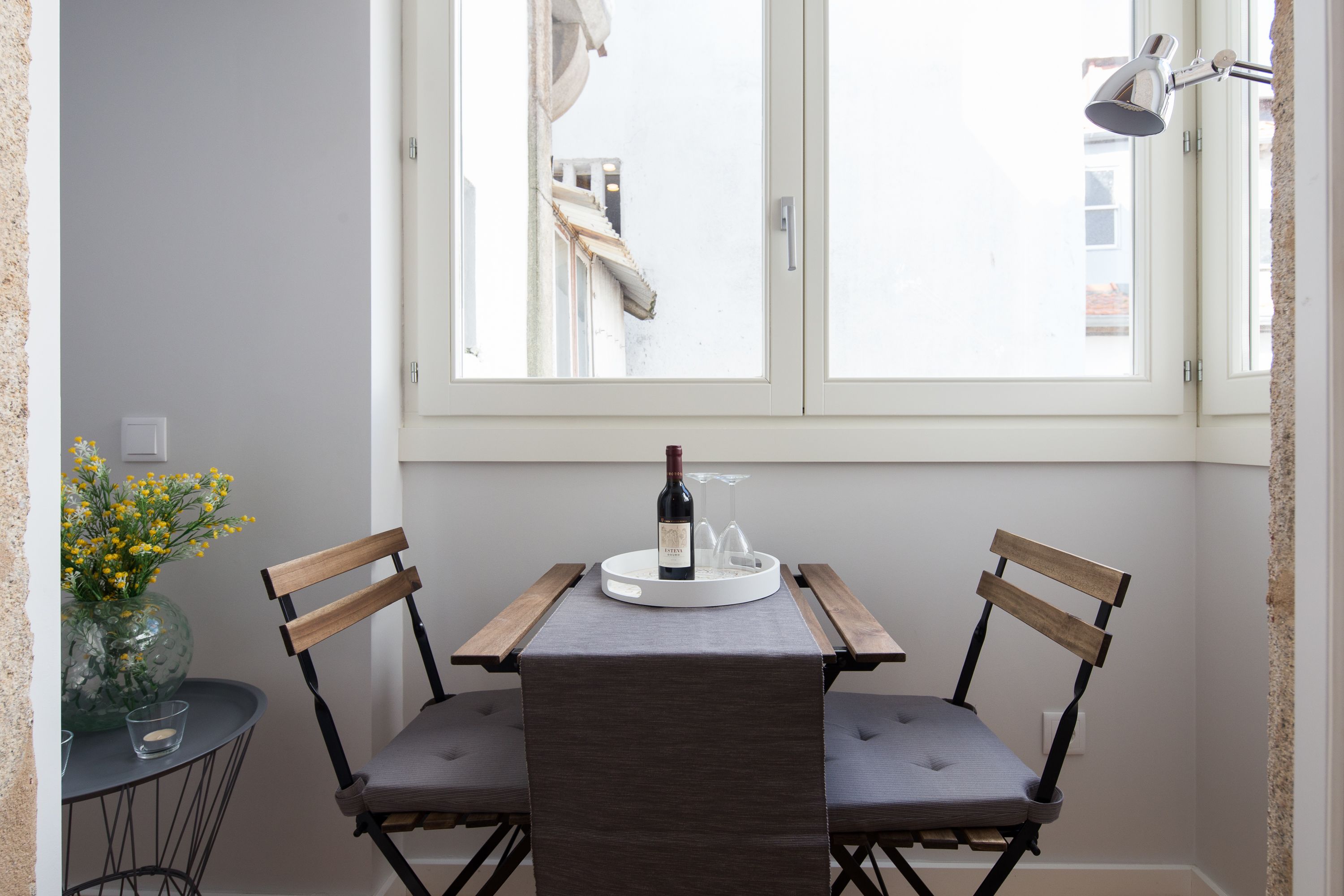 A small dining area with two wooden chairs, a table with a wine bottle and glass, and a vase with yellow flowers.
